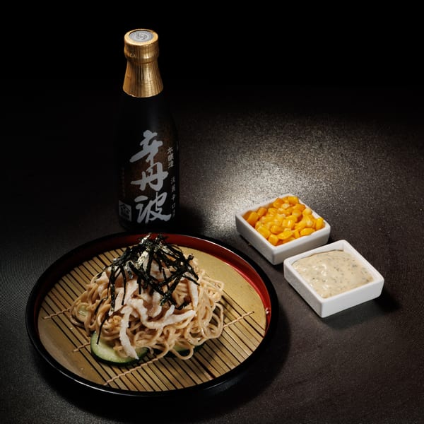 Kogane Ramen's cold ramen with seaweed, fried toppings, cucumber, corn, and sauce, next to a sake bottle.