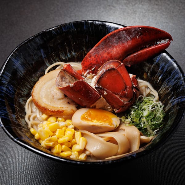 Kogane Ramen's lobster ramen with pork, corn, egg, and green onions in a dark bowl.