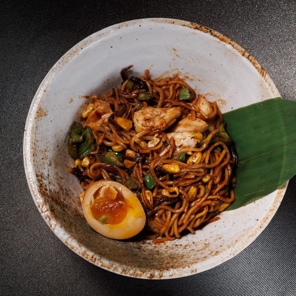 Kogane Ramen's chicken yakisoba with a soft-boiled egg and a green leaf garnish in a rustic bowl.