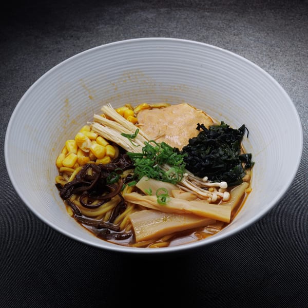 A bowl of Kogane Ramen with noodles, corn, mushrooms, seaweed, and tofu in broth.