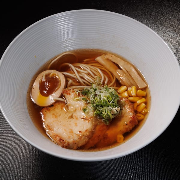 A bowl of Kogane Ramen with noodles, pork, egg, corn, bamboo shoots, and green onions.