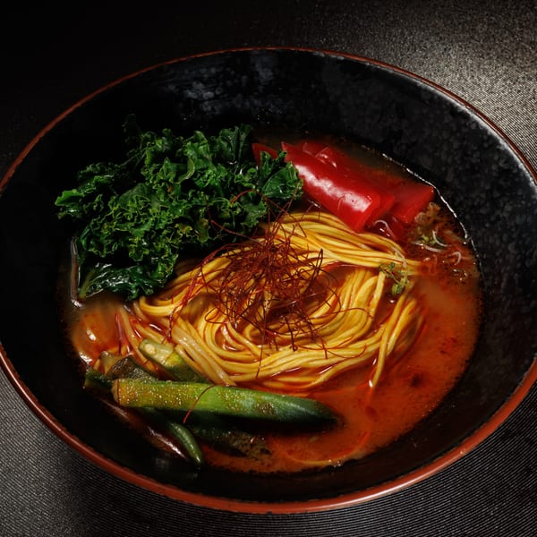 Kogane Ramen's spicy ramen with noodles, kale, red peppers, okra, and chili threads in a black bowl.